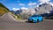 Cool baby blue Ford Focus RS drives into a hairpin turn in the sunny mountains.