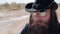 A cool cowboy in a black hat and glasses with a beard looks into the distance in the desert