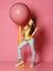 Cool and fashion teen girl in jeans and yellow t-shirt stepped on big pink balloon yellow tape, drinks yellow juice and wave to us
