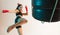 Cool female fighter trains kicking with punching bag made of tires in neon studio light. Women`s sport workout