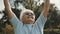 Cool grandmother with pink sunglasses and headphones stretching in the park. Recreation in old age.