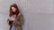 Cool hipster teen girl red hair standing on city urban street using cell phone.