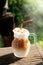 Cool ice caramel macchiato coffee on rough wooden table in topical garden.