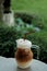 Cool ice caramel macchiato coffee on rough wooden table in topical garden.