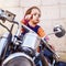 Cool little biker girl playing and having fun on fashioned motorcycle. Humorous portrait of child points to the road with finger