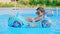 Cool little boy sunbathe in blue street pool in courtyard. Joyful toddler, baby in inflatable car toy. Child chilling in