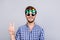 Cool! Playful young brunette bearded man in three pairs of bright colorful glasses and checkered casual shirt is fooling around, p