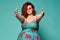 Cool plus-size overweight redhead lady in sunglasses shows a gesture sign finger - gun, aimed at us on mint