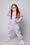 Cool red-haired kid girl in glasses and pink jumpsuit with zipper and big pockets stands with legs wide apart