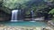 A cool refreshing waterfall pouring into an emerald pond hidden in a mysterious forest of lush greenery