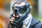 Cool shooter with handgun in paintball helmet aiming in camera.