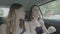 Cool teen girls sitting on backseat of riding car dancing in the rhythm of music during the road trip -