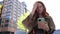 Cool teen redhead girl sitting on big city urban street using smartphone.