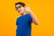 Cool teenager boy in a blue shirt and glasses shows his hand a class on a yellow background with copy space