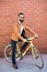 Cool young bearded hipster besides a fixie bicycle on brick wall on the street