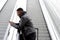 Cool young black man traveling with mobile phone and bag on escalator