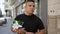 Cool young latin man standing on a sunny city street, looking at his watch, hand grasping a bouquet of vibrant spring flowers