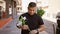 Cool young latin man standing on a sunny city street, looking at his watch, hand grasping a bouquet of vibrant spring flowers