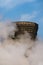 Cooling tower, covered in fog, in front of a blue sky