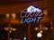 Coors Light beer neon sign with rustic Canadian wooden cabin in the background.