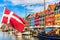 Copenhagen iconic view. Famous old Nyhavn port in the center of Copenhagen, Denmark during summer sunny day with Denmark flag on