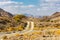 Copper Hike trail, winding gravel dirt road through Wadi Ghargur riverbed and rocky limestone Hajar Mountains in Hatta, UAE