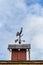 Copper rooster weathervane on top of red rooftop cupola with a blue sky and white clouds in the background