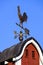 Copper weathervane on red barn cupola, blue sky background.