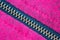 Copper zipper crossing in diagonal over a magenta and black fabric