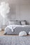Copy space on the empty grey wall of contemporary bedroom with king size bed and bunch of white balloons above golden nightstand