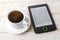 Copy space on a screen of e-book reader near cup of hot coffee on a white wooden table. E-reading for pleasure and education