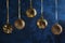 Copy space on a textured dark blue background. Five golden Christmas balls hanging from ribbons. Festive layout.