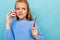 Copyspace photo of charming pensive schoolgirl with a toothbrush and dental mockup on blue wall background