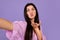 Coquette armenian woman taking selfie, blowing air kiss on purple studio background, making photo of herself
