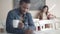 Coquette young Caucasian woman smiling and waving to African American blurred man sitting at front in lunchroom