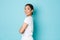 Coquettish pretty asian girl in white t-shirt standing in profile and turning right with curious smiling face, looking