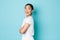 Coquettish pretty asian girl in white t-shirt standing in profile and turning right with curious smiling face, looking