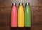 Coral pink, green chive, yellow sunlight or saffron color of steel thermo eco bottle for liquid on wooden table, sprayed with wate