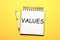 Core values. Stylish open notebook and pen on yellow background, top view