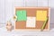 Corkboard for notes with empty paper sheets on a wooden table and next to a clay jar with daisies