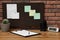 Corkboard with pinned notes hanging on brick wall over desk in office