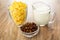 Corn flakes in glass, bowl with dried grape, pitcher with yogurt on table