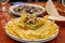 Corn nachos with melted cheese, avocado guacamole, onion and chopped tomato served on a table in a Mexican restaurant