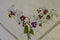 Corner with a border for embroidery of a bouquet with brown and purple pansies with small blue flowers on branches with leaves