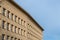 Corner of a building against blue sky. Beige plaster, simple, linear cornice and row of windows