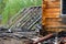 A corner of a burned-out wooden house with a window and a greenhouse roof next to yellow wood and black charred logs