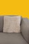 Corner fragment of beige grey upholstered couch with velour decorative cushion on sand yellow wall background. Modern interior