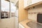 Corner of a small kitchen with white base units and walls with wooden details on the countertop and cornices and aluminum window