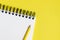 Corner of a spiral bound notepad / sketchpad on a yellow background, with a yellow pencil and space for copy