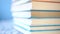 Corner of a stack of multi-colored books in hard and soft cover on a blue bright background